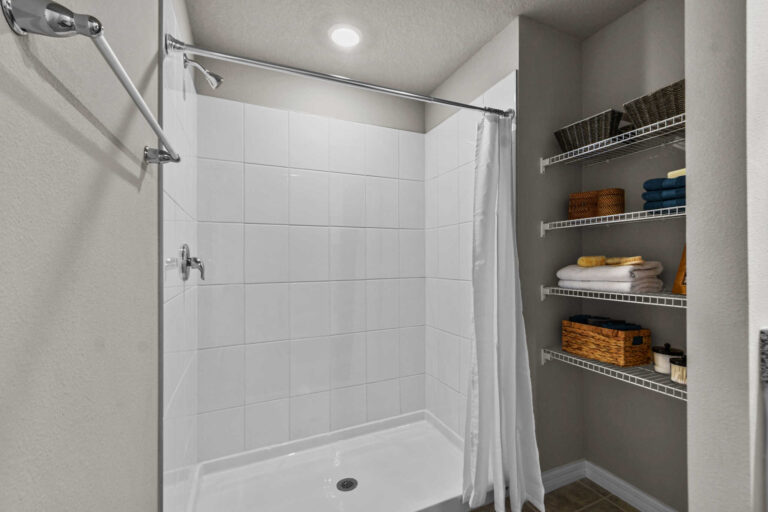 Bathroom with walk-in shower next to towels and other bathroom amenities on shelves