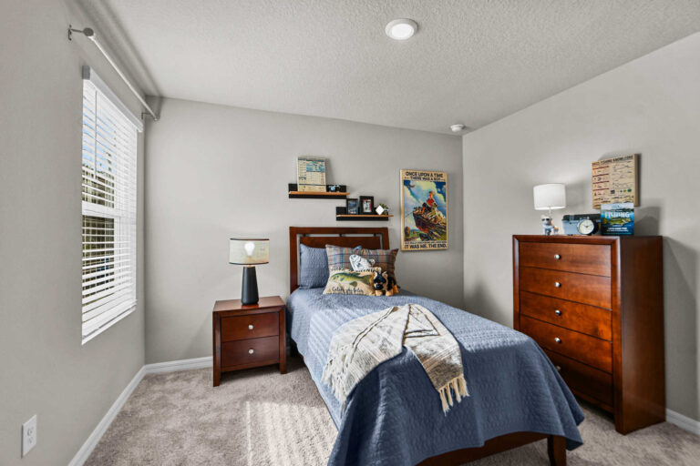 Single bedroom with twin-size bed, dresser, side table with drawers, and floating shelves